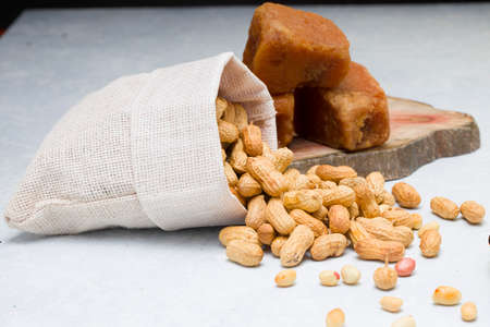 Peanut in nutshell which is very healthy , arranged in a burlap sack which is spilled out on a white textured background with jaggery placed nearby,selective focus.の写真素材