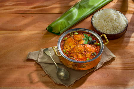 Seer Fish curry, traditional Indian fish curry ,kerala special ,arranged in a copper serving bowl with a bowl of cooked rice and banana leaf for serving food,arranged on wooden   textured background,isolated.の写真素材