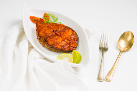 Seer fish fry arranged beautifully and garnished with onion, lemon and tomato slices on white...