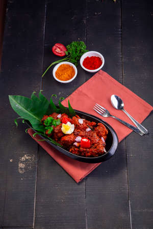 Chicken peralan or chicken dry curry, kerala special chicken dish which is beautifully arranged in a black tableware in oval shape and lined with banana leaf and garnished with flower shaped egg and shallots placed on black background with table clothの写真素材
