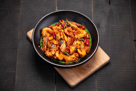 Kerala style Prawns roast or chemmeen varattiyathu  made using red kashmiri chilli flakes and coconut slices as main ingrediants and garnished with onion rings and tomato slices ,placed on a black textured background.の写真素材