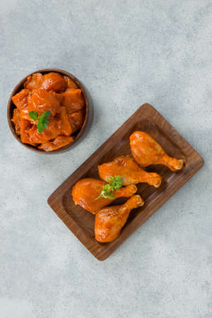 Raw marinated chicken cubes and legs arranged in a wooden tableware garnished with fresh coriander leaf  and mint leaf which is placed on grey white textured background.の写真素材