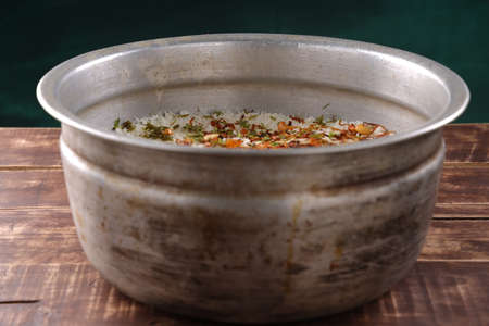 Dum chicken biriyani, close up image of Kerala-Thalassery biriyani garnished with fried onion,cashew nut,raisens and coriander leaf which is arranged in a big aluminium cooking pot which is placed on wooden textured background.の写真素材