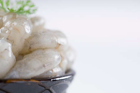 Raw peeled prawns or shrimp arranged in a black ceramic small pot and garnished with coriander leaf which is ready to cook ,placed on a white textured background.の写真素材