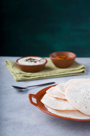 South Indian traditional  breakfast Dosa or Thattu dosa made using cast iron dosa thawa, arranged in a tableware with side dish white coconut chutney and onion chutney on white textured background.の写真素材