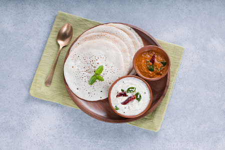 South Indian traditional  breakfast Dosa or Thattu dosa made using cast iron dosa thawa, arranged in a tableware with side dish white coconut chutney and onion chutney on white textured background.の写真素材