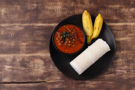 Puttu,Raw rice puttu,Arisi Maavu Puttu with chana or kadala curry, Bengal gram cuirry _breakfast items made using raw rice flour, an ideal combination arranged in a black plate with wooden backgroundの写真素材