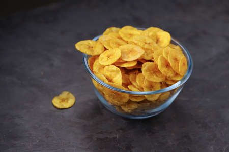Dried banana chips or banana waffers,arranged beautifully in a glass bowl with grey  textured...