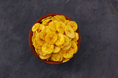 Dried banana chips or banana waffers,arranged beautifully in a clayor earthenware with grey textured background, isolated.の写真素材