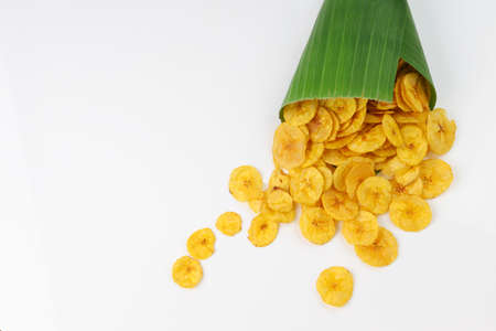 Dried banana chips or banana waffers spilled out from the banana leaf cone to the white textured background.の写真素材
