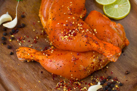 Marinated  chicken leg without skin arranged in a wooden base and garnished with lemon slices ,spices, coriander leaves, garlic cloves and pepper on graphite textured backgroundの写真素材