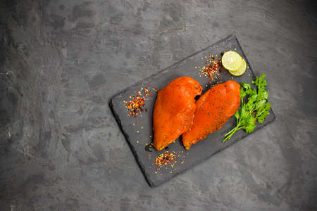 Marinated chicken breast fillets arranged on a graphite board and garnished with lemon slices, chilli flakes,pepper balls and  coriander leaves on grey  textured background.の写真素材