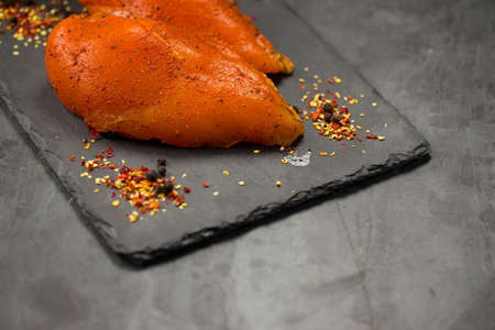 Marinated chicken breast fillets arranged on a graphite board and garnished with lemon slices, chilli flakes,pepper balls and  coriander leaves on grey  textured background.の写真素材