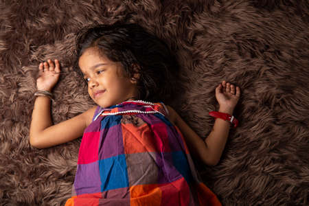 A girl child showing different gestures who is lying on a synthetic rug which brown in colour,isolated.の写真素材