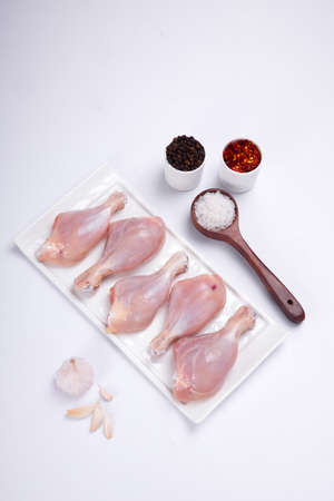 Raw chicken drum sticks arranged on white table ware with black pepper,chilli flakes,salt and garlic on white colour backgroundの写真素材