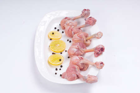 Raw chicken lollipop,ten pieces of chicken lollipop arranged on a serving white plate with lemon slices and black pepper on white coloured backgroundの写真素材