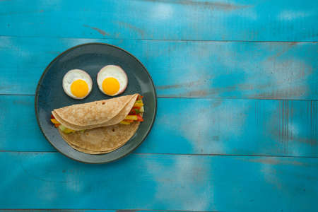 Chapati,healthy food made of wheat flour and it is stuffed with vegetables and eyes are made of half boiled eggs and it is arranged in aqua rustic ceramic plate with blue textured  background.の写真素材