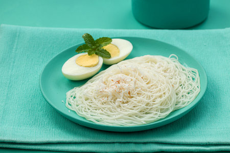 Ideyappam or noolappam,south Indian breakfast item  which is arranged beautifully with two slices of boiled eggs in an aquamarine colour tableware placed on a solid aquamarine colour background,isolated.の写真素材