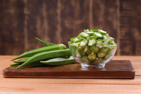 Okra or Lady's finger or Bhindi fresh green vegetable arranged  on a wooden board with a glass bowl...