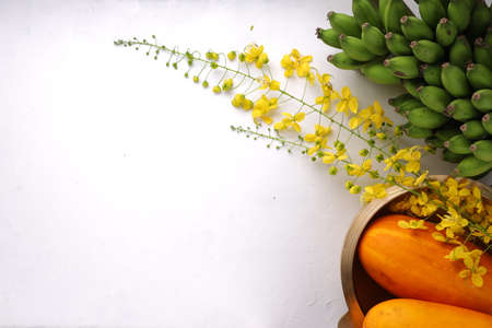 Golden shower flower,yellow cucumber and raw banana bunch arranged on a white surface with grey...