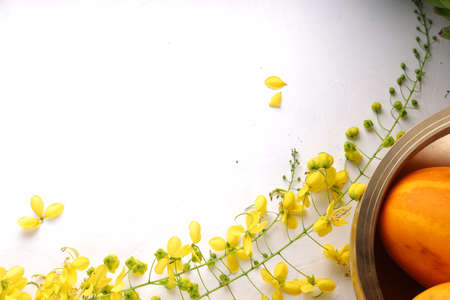 Golden shower flower,yellow cucumber and raw banana bunch arranged on a white surface with grey textured background and a brass traditional vessel or urule arranged in the background.の写真素材