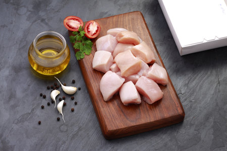 Raw chicken tender fry cut without skin arranged on wooden board and garnished with oil,coriander leaf,tomato slices,garlic and pepper with packaging box on stone textured  backgroundの写真素材