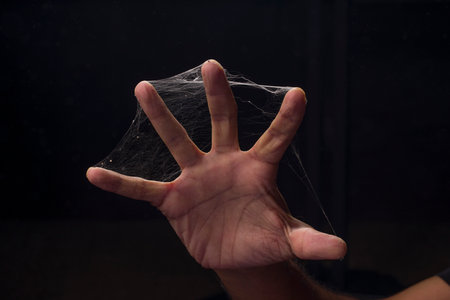 A man fingers covered with spider web on black background