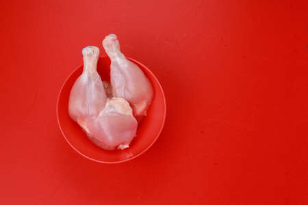 Raw whole chicken leg or thigh without skin arranged in a red bowl on a red solid colour backgroundの写真素材