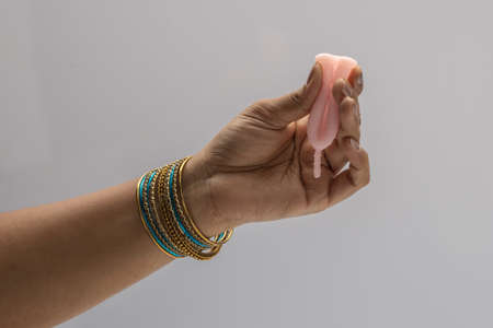 An Indian woman hand holding reusable silicon Menstrualcup  and showing different types of folding.