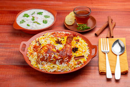 Chicken dum biryani ,Hydrabadi chicken biryani with basmathi rice and raita as side dish and hot lemon tea  with wooden background or texture,selective focusの写真素材