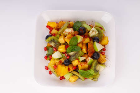 Mixed fruit salad arranged in a white tableware and garnished with mint leaf.