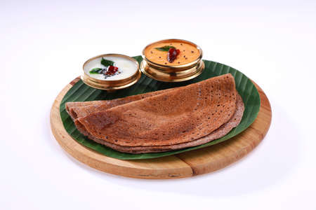 Ragi Dosa, healthy south Indian breakfast item arranged on a round wooden base lined with banana leaf and coconut chutney placed beside it.の写真素材