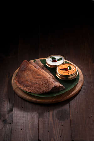 Ragi Dosa, healthy south Indian breakfast item arranged on a round wooden base lined with banana...