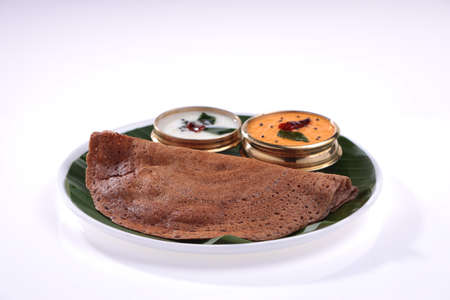 Ragi Dosa, healthy south Indian breakfast item arranged on a round wooden base lined with banana leaf and coconut chutney placed beside it.の写真素材