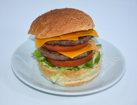 Big hamburger on a white plate isolated on a white background. close up of double cheese burger with cheddar cheese served on plateの写真素材