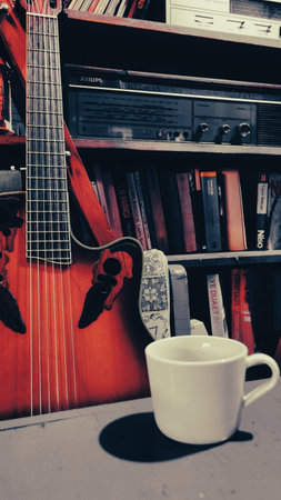 Coffee cup and guitar on the shelf in the library.