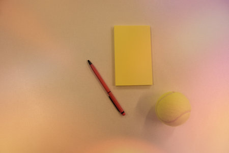 Tennis ball and notepad with red pen on white background.