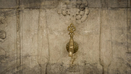 Brass faucet on a fountain with patterned marble wall in the old Ottoman traditional style. Vintage public fountain wallpaperの写真素材