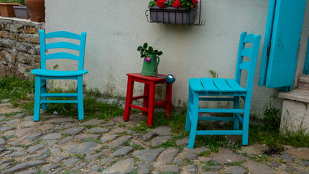 Blue chairs and wooden red stool against a home wall in Gliki, an old Greek village in Gokceada. Canakkale, Turkey. There's a flower pot with red flower on the small stool tableの写真素材