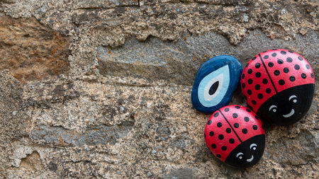 Colorful wooden ladybugs and evil eye bead icon on old stone wall background with copy spaceの写真素材