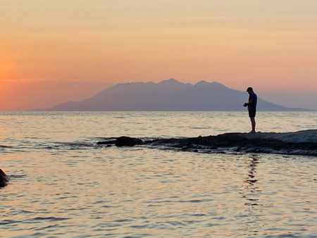 Silhouette of a man standing on a rock and watching the sunsetの写真素材