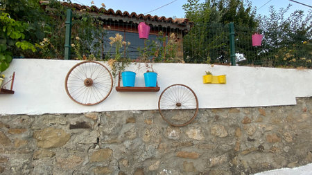 Flowers in metal pots hung on the garden wall and decoration elements hung on the wall. Ornaments hung on the walls in the streets of Aegean village.の写真素材
