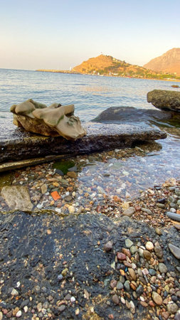 A rock formation freshly removed from the sea that has taken many different shapes under the influence of the sea waves. Seashore and mountain view at the backgroundの写真素材