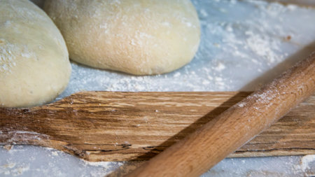 Preparation of raw dough balls with a rolling pins for cooking pastries on a marble counter with...