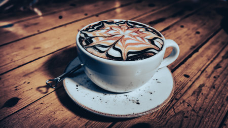 A cup of cappuccino with a beautiful latte art pattern on a vintage brown table.の写真素材