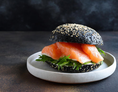 Black burger with salmon, arugula and sesame seeds on a dark backgroundの素材