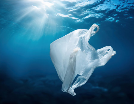 Plastic bag floating underwater in deep blue ocean. Concept of environmental pollutionの素材