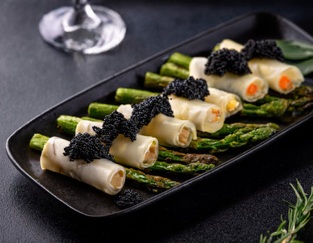 Stuffed asparagus rolls with black caviar on black plateの素材