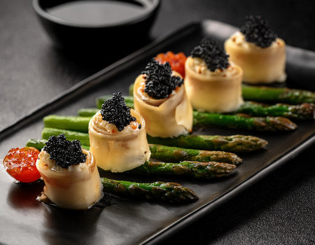 Asparagus rolls with black caviar on a black plate.の素材