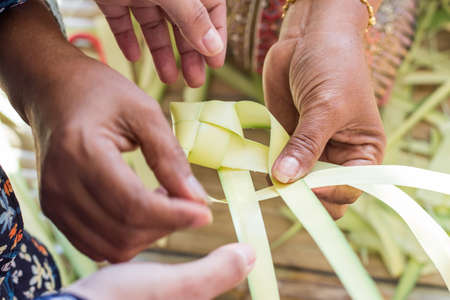 Handcrafting concept. Asian mom teaches her daughter how to make fish from coconut leaf. Thai...
